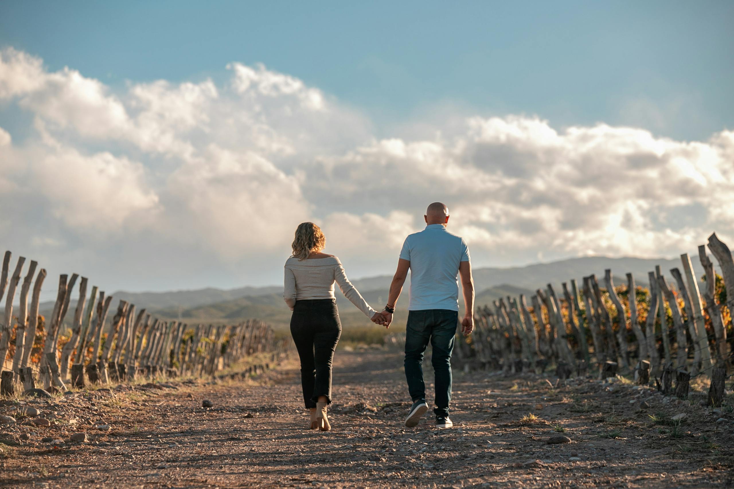 Back View of Couple Walking Together between Fields and Hills