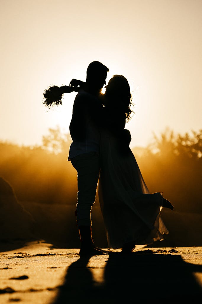 Side view silhouettes of happy young couple hugging each other while relaxing on sandy beach during date at sunset